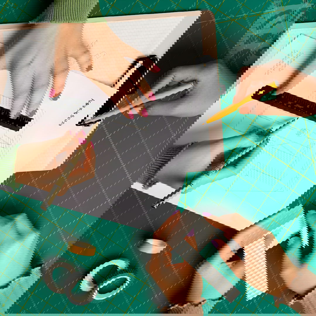 Hands working on a crafting project with ruler and paper